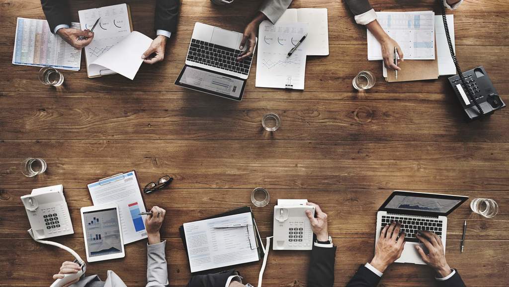 Aufnahme von oben: Meetingtisch mit Laptops, Gläsern und Papieren
