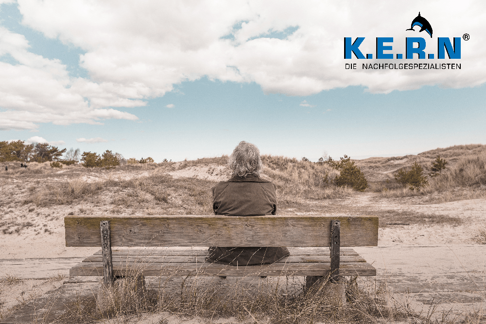 Senior sitzt auf einer Bank in den Dünen der Ostsee, oben rechts das KERN Logo