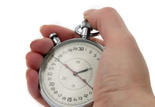 Eine Hand hält eine alte analoge Stoppuhr in der Hand. Der Stopper steht auf 25s