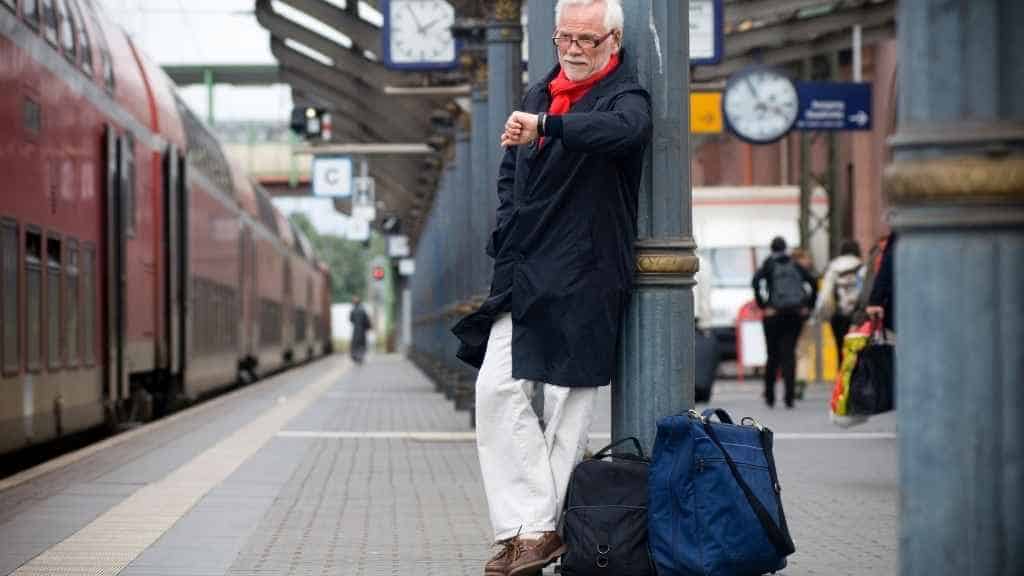 Ein Mann steht auf dem Bahnhof und schaut auf seine Armbanduhr.